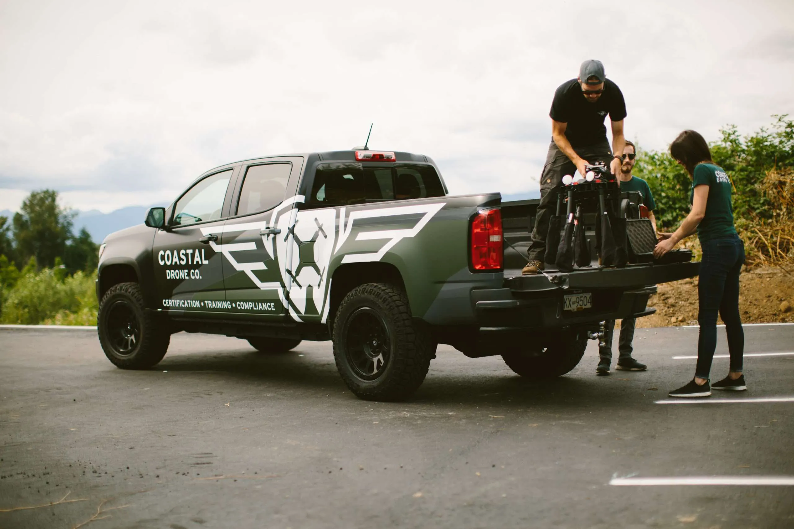 Coastal Drone team lifting a large multirotor drone from the tailgate of a branded pickup truck