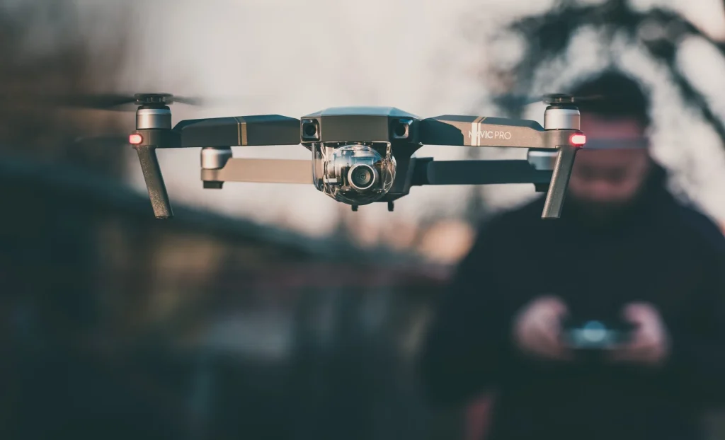 DJI Mavic Pro hovering in the foreground while a pilot flies it using a handheld controller